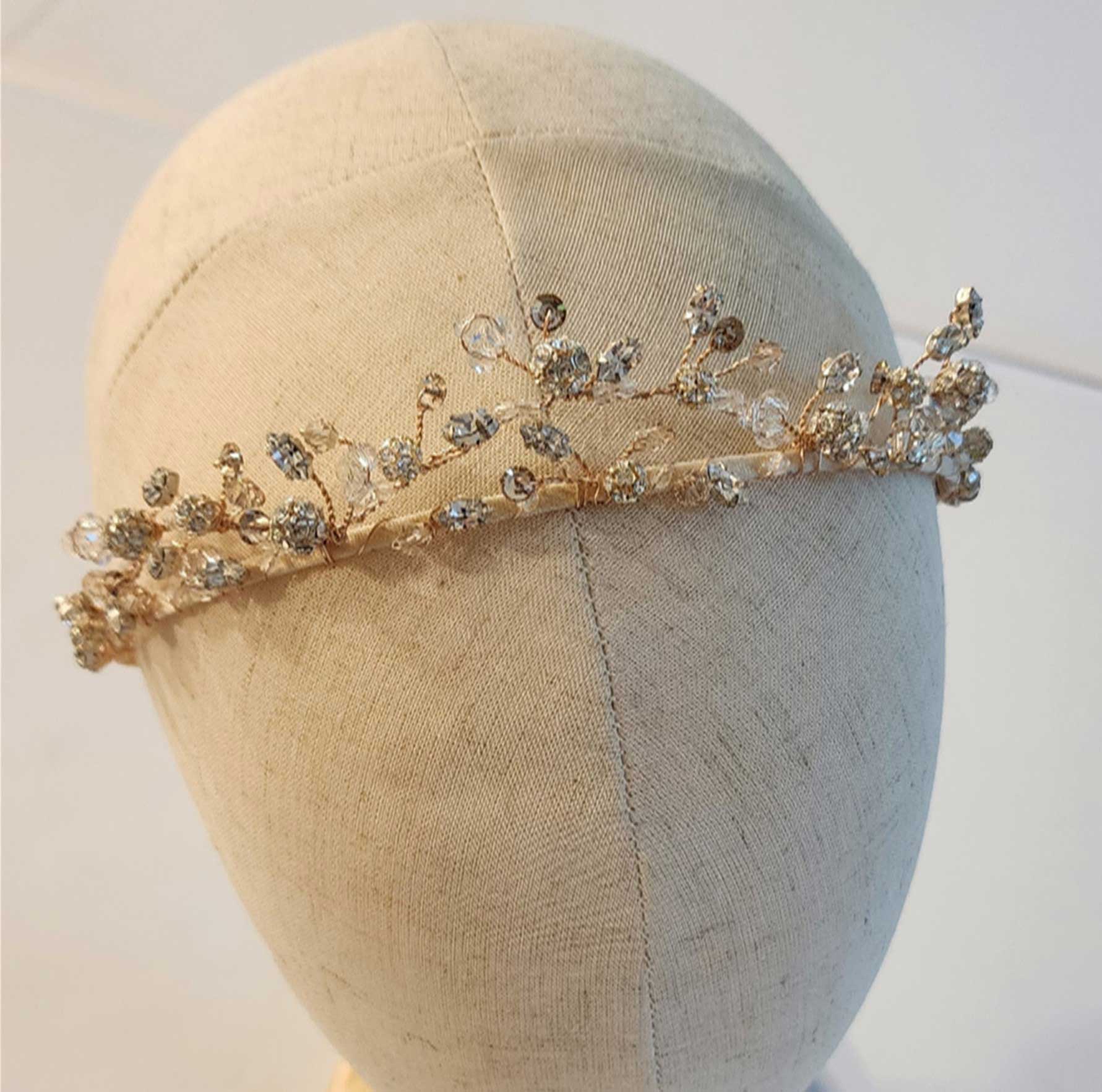 Delicate gold-tone wire headpiece with clear beads and branching details displayed on a fabric mannequin head.